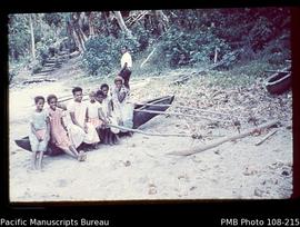 [Girls seated on beached outrigger canoe]