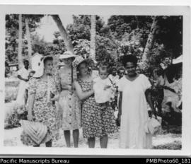 Three European women, a baby and a ni-Vanuatu woman, villagers in the background