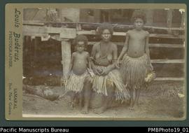 Mounted photograph of Papua New Guinean woman and two girls in front of a dwelling.