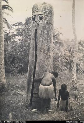 Woman and child with large carved wooden slit drum, South West Bay Malekula