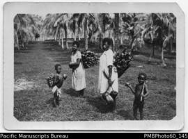 Two ni-Vanuatu women carrying wood and coconut alongside two children