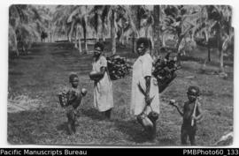 Two ni-Vanuatu women carrying wood and coconut alongside two children