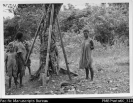 ni-Vanuatu women and children standing around a tree and bamboo