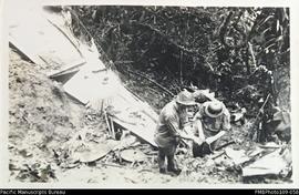 RNZAF officers prepare to blow up three unexploded depth charges near wing of the wrecked plane, ...