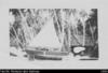 Outrigger canoe "The Marjorie" raised up on crates; Man in helmet standing in backgroun...
