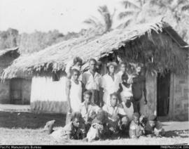 Group of men, women, and children outside dwelling, probably South West Bay, Malekula