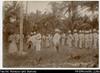 Two men (including Woodford?) and Clara Austin standing by flagpole with naval officers and soldi...