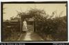 European woman (Mrs. Woodford?) standing by gate. Written on back in ink: 'Our front gate. Bougai...