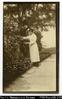 European woman (Mrs. Woodford?) standing on garden path, picking flowers. Written on back in ink:...