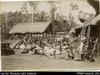 View of a village with villagers seated in clearing behind luggage and luggage-bearing sticks. Eu...