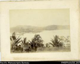 Board-mounted photograph of harbor with ship and European settlement in background. Appears to be...