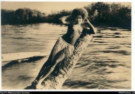 No label. Kwato Island Girl posing on the trunk of a dead coconut tree with river in background.