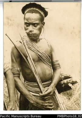 Young man in traditional bilas (dress) holding a bow and arrows with a bundle of sugarcane cuttin...