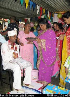 [Suva Wedding  Women giving gifts to Mahen the groom. Bride's mother in pink next to groom.]