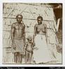 Solomon Islands man, woman and child in front of pandanus dwelling. Foliage with dwelling and pat...