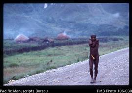 [Dani man walking on the road to Wamena; arms wrapped for warmth]