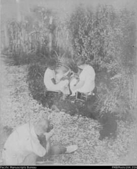 Women and children sitting in a garden being photographed by E.O. Cox