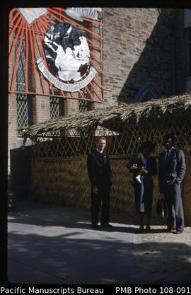 [Neilson Whyte with Tele, Serei and child in front of Australian Presbyterian Missions sign]