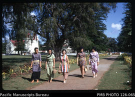 'Female Premier's Office staff walking alongside the Pangai, with Royal Chapel and Palace in back...