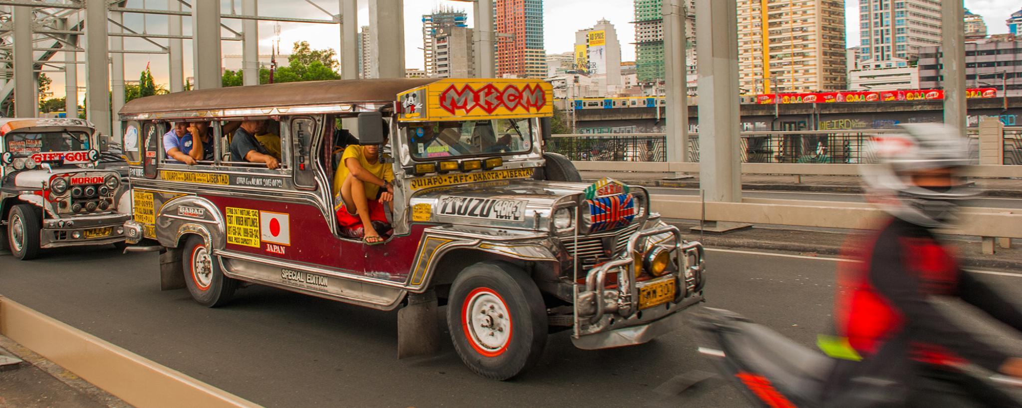Jeepney bus travelling on a street with buildings in the distance