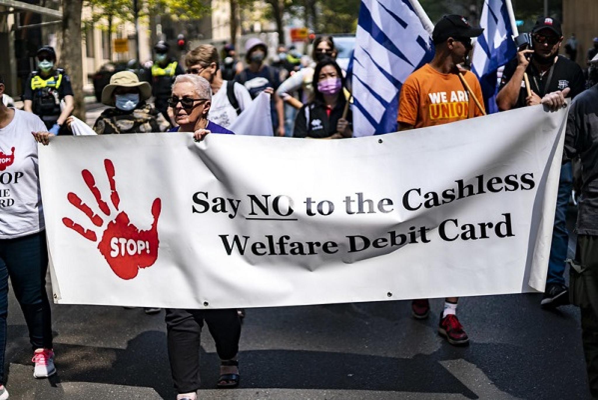 Image of banner opposing the Cashless Welfare Debit Card at a 2021 ‘Demand a Living Wage for all’ rally in Melbourne, Victoria, by Matt Hrkac on flickr https://flic.kr/p/2kMhtEh, free to use under CC BY 2.0 DEED licence 