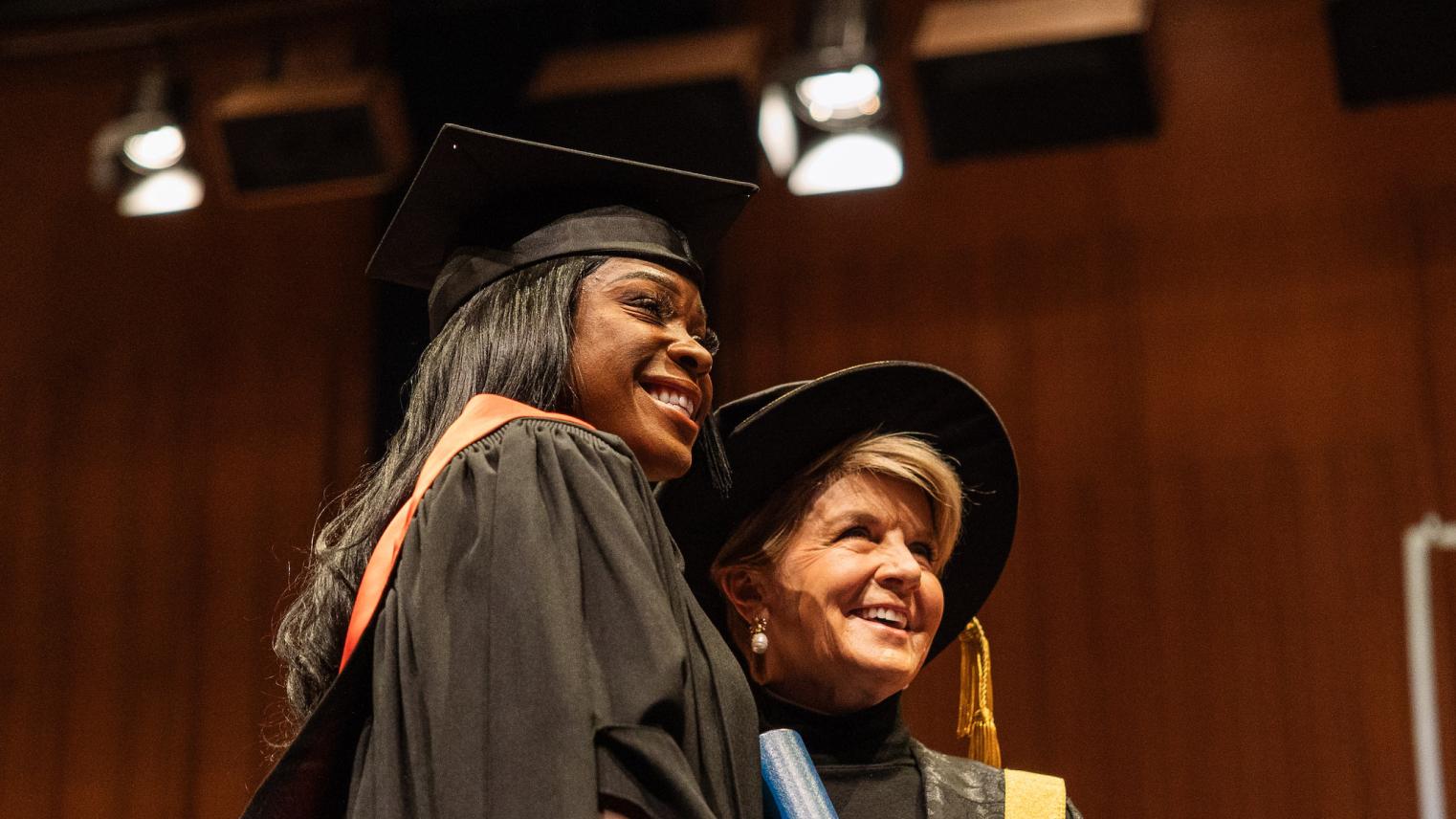 Precilla Anna-Kaii Lawrence and Julie Bishop at the 2023 Mid-Year Graduation Precilla Anna-Kaii Lawrence standing on stage with Julie Bishop in graduation robes, holding her Testamur
